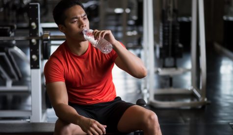 Young Asian strong muscular man drink water in fitness gym. He break from working out exercise. Bodybuilding and healthy lifestyle concept